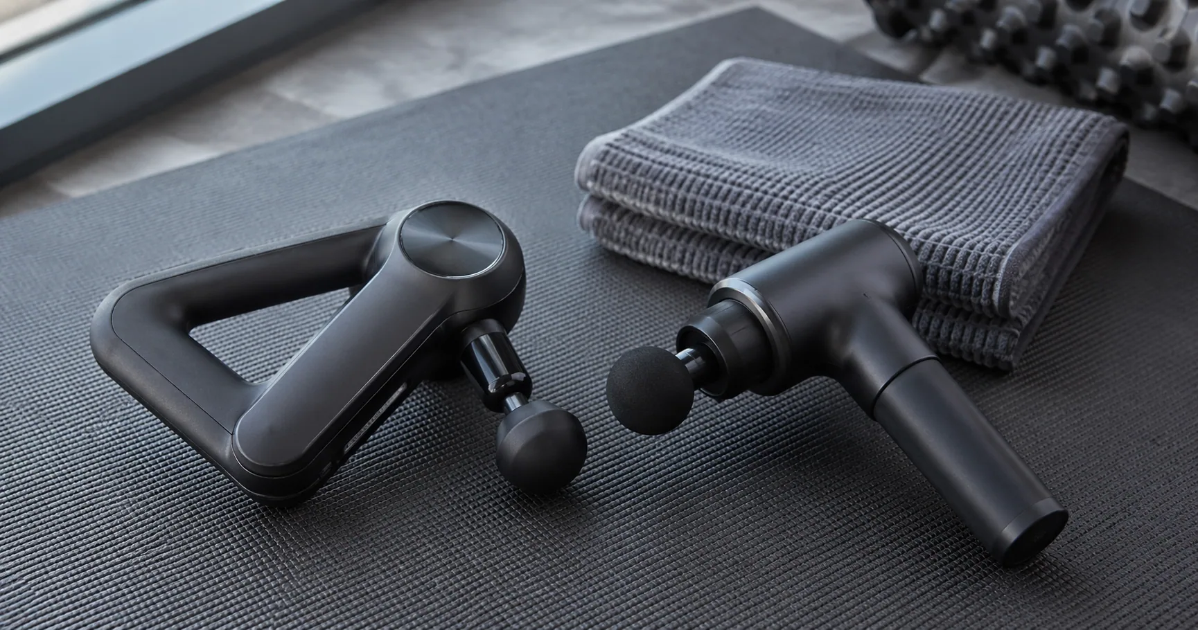 Theragun Prime and Hypervolt 2 Pro percussion massagers side by side on a gym bench