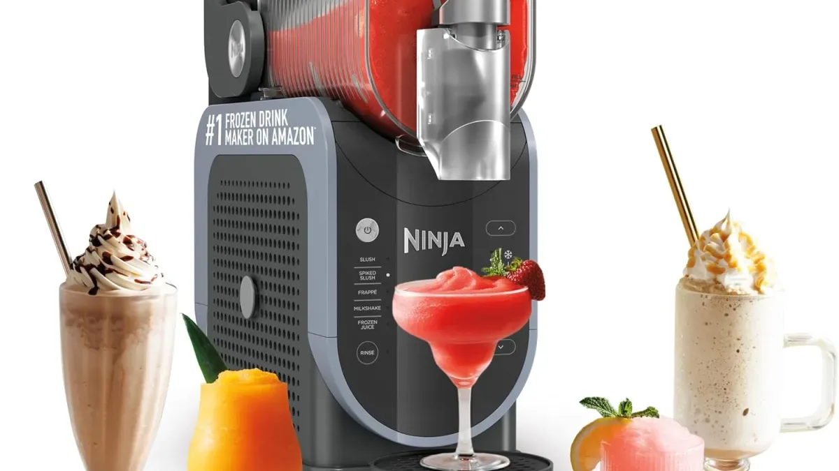 Frozen drink maker on a marble kitchen counter pouring a red slushie, with two icy frozen drinks beside it